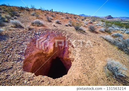 Desert Sinkhole and Rugged Terrain in Harsh Sunlight with Distant Nevada Mountains Desert Sinkhole and Rugged Terrain in Harsh Sunlight with Distant Nevada Mountains 131563214