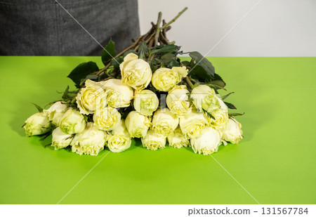 A florist holds a bundle of cream roses together over a green table. The flowers are fresh and ready to be tied or wrapped. 131567784