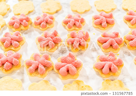 Rows of flower-shaped cookies piped with raspberry buttercream are lined up for assembling Easter Cookie Sandwiches with Raspberry Buttercream. 131567785