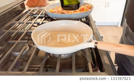 A ceramic frying pan with wooden handle is preheating on a gas stove. The flame is visible underneath as part of breakfast preparation. A ceramic frying pan with wooden handle is preheating on a gas stove. The flame is visible underneath as part of breakfast preparation. 131567821