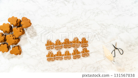 Gingerbread girl cookies are evenly spread out in rows, surrounded by tools and supplies for decorating. Gingerbread girl cookies are evenly spread out in rows, surrounded by tools and supplies for decorating. 131567838