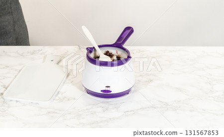 Preparing chocolate for dipping; a melting pot with chocolate placed on a marble countertop alongside dipping tools, ready to coat peppermint cut-out sugar cookies. 131567853