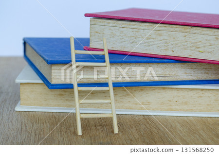 Books on a wooden desk with wooden ladder under natural daylight emphasizing peaceful study time. Books on a wooden desk with wooden ladder under natural daylight emphasizing peaceful study time. 131568250