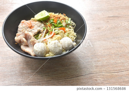 dry Chinese egg yellow noodles topping boiled chop pork with pork ball dressing cayenne pepper couple shrimp on bowl 131568686