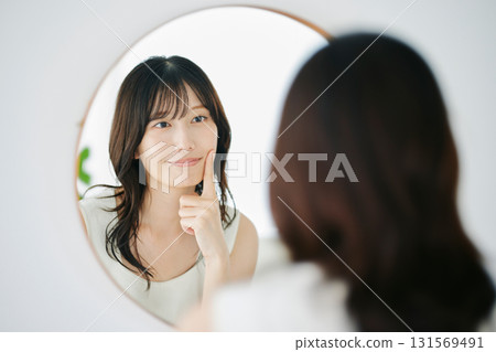 微笑的女人對著鏡子檢查自己的皮膚狀況 131569491