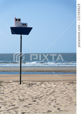 Wooden model of boat on pole on sandy beach with real big cargo ship in background, sunny day Wooden model of boat on pole on sandy beach with real big cargo ship in background, sunny day 131569829