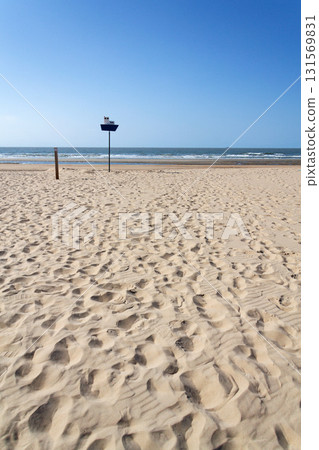 Wooden model of boat on pole on sandy beach with real big cargo ship in background, sunny day 131569831