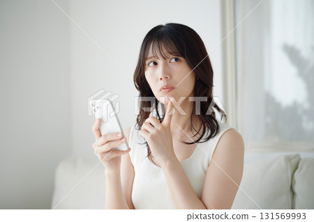 A woman sitting on a couch and operating a smartphone A woman sitting on a couch and operating a smartphone 131569993