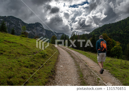 Young Man With Backpack Hiking On Gravel Pathway Toward High Mountains In Tyrol, Austria Young Man With Backpack Hiking On Gravel Pathway Toward High Mountains In Tyrol, Austria 131570851