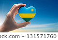 Heart shaped Rwandan flag held by hand against blue sky 131571760