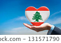 Lebanese flag heart shape and blue sky held by hand 131571790