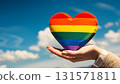 Hand holding a rainbow flag with a heart shape and blue sky 131571811