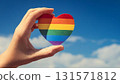 Hand holding a rainbow flag with a heart shape and blue sky 131571812