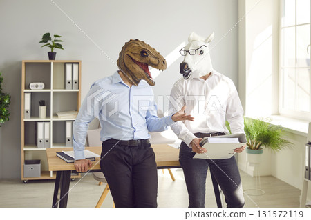 Two young workers in funny lizard and horse masks standing by office desk and talking 131572119
