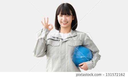 一位身穿工作服的年輕女子拿著頭盔,擺出「OK」姿勢 一位身穿工作服的年輕女子拿著頭盔,擺出「OK」姿勢 131572162