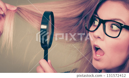 Woman holding magnifying glass looking at hair Woman holding magnifying glass looking at hair 131572412