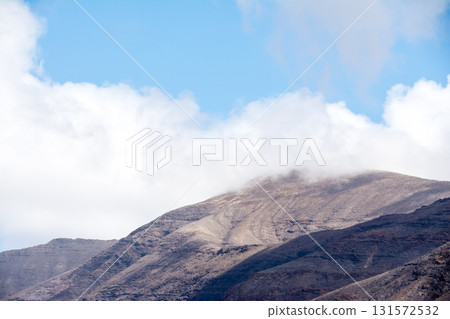White clouds hang over the rock formations and bare mountains on Fuerteventura in the Canary Islands 131572532