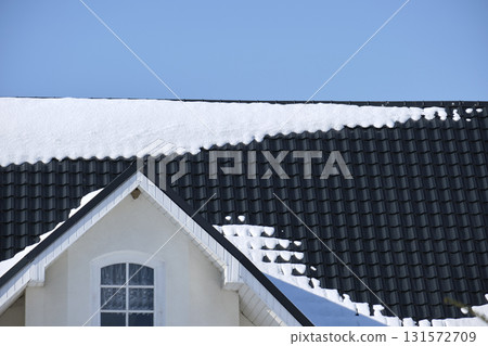 Closeup of house roof top covered with snow in cold winter. Tiled covering of building in wintertime weather Closeup of house roof top covered with snow in cold winter. Tiled covering of building in wintertime weather 131572709