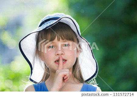 Close-up portrait of serious little girl in a big hat. Child having fun time outdoors in summer. Close-up portrait of serious little girl in a big hat. Child having fun time outdoors in summer. 131572714