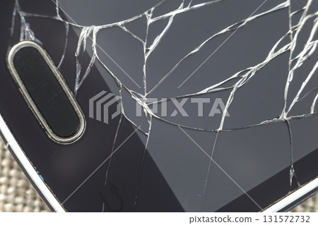 Close-up detail of black old cellphone with cracked screen on light cloth background. Gadget repair and maintenance concept. Close-up detail of black old cellphone with cracked screen on light cloth background. Gadget repair and maintenance concept. 131572732