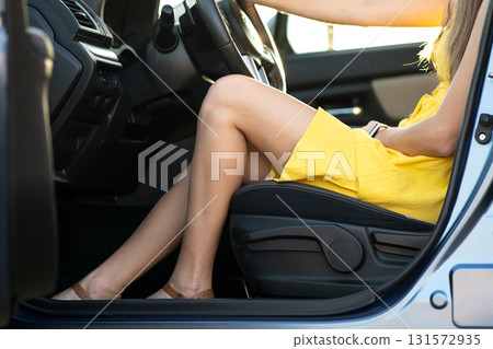 Close up of young woman driver with long legs in yellow summer dress behind steering wheel driving a car. 131572935