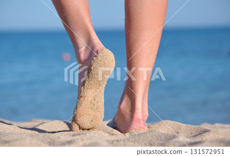 Close up of female feet walking barefoot on white grainy sand of golden beach on blue ocean water background 131572951