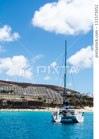Yachts in the emerald green sea, white-walled buildings beside the white sandy beach, and a bare mountain in the distance - Fuerteventura Yachts in the emerald green sea, white-walled buildings beside the white sandy beach, and a bare mountain in the distance - Fuerteventura 131573052