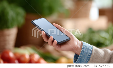 Focused person shopping with smartphone in hand at grocery market. Using digital app for payment or list, showcasing modern retail technology in store Focused person shopping with smartphone in hand at grocery market. Using digital app for payment or list, showcasing modern retail technology in store 131574389