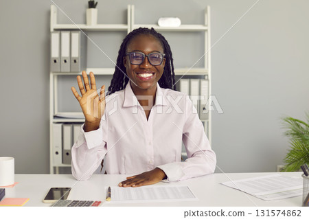 Portrait of happy, smiling African American business woman waving hand at online work meeting Portrait of happy, smiling African American business woman waving hand at online work meeting 131574862