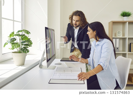 Male accountant helping his female colleague with data sheets on the office computer 131574863