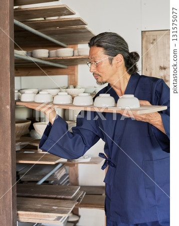 A male potter arranging molded pottery on a shelf A male potter arranging molded pottery on a shelf 131575077