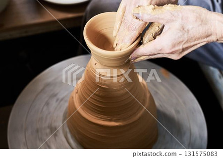 A potter using a potter's wheel to shape a vessel 131575083