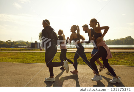 Group of sporty smiling people in sportswear jogging together in the park at sunset. 131575371