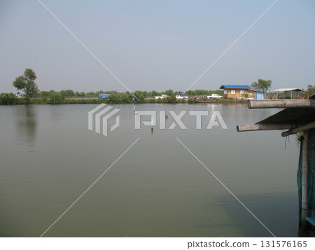 Fishing pond lake calm water rural house waterfront wooden dock blue roof tree sky reflection Fishing pond lake calm water rural house waterfront wooden dock blue roof tree sky reflection 131576165