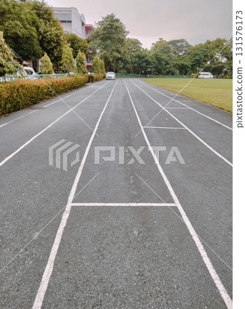 Running track lane marking leading toward school building entrance and green field under overcast sky with calm atmosphere 131576173