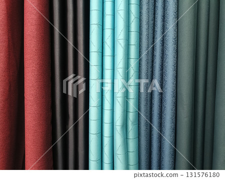Curtain fabric display vertical rolls showing red, dark brown, turquoise patterned, blue textured and teal textiles arranged neatly with soft folds and varied textures, inviting tactile curiosity 131576180