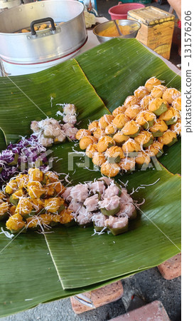 Traditional Thai dessert served on banana leaf with shredded coconut and colorful sticky rice bites arranged in clusters, warm market setting and rustic cookware Traditional Thai dessert served on banana leaf with shredded coconut and colorful sticky rice bites arranged in clusters, warm market setting and rustic cookware 131576206