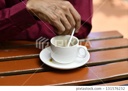 Man stirring hot cup of coffee on wooden outdoor table, casual morning moment with warm tones and relaxed mood Man stirring hot cup of coffee on wooden outdoor table, casual morning moment with warm tones and relaxed mood 131576232