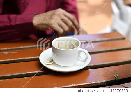 Empty white coffee cup on saucer with teaspoon on wooden table, hand blurred in background conveying calm morning moment Empty white coffee cup on saucer with teaspoon on wooden table, hand blurred in background conveying calm morning moment 131576233