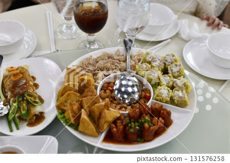 Festive platter of assorted Chinese dim sum and appetizers on round serving tray with dipping bowl and iced drinks, inviting family meal and celebration scene Festive platter of assorted Chinese dim sum and appetizers on round serving tray with dipping bowl and iced drinks, inviting family meal and celebration scene 131576258