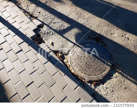 Sewer Manhole on the Street Near Sidewalk Showing Wear and Surrounding Pavement 131577850