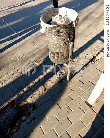 Trash Can on the Street Surrounded by Shadows Reflecting Early Morning Light 131577851