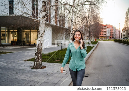Young woman walking down the street while talking on smartphone 131578023