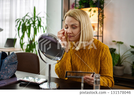Woman applying makeup in cozy indoor setting during bright daylight, enjoying her self-care routine with natural light streaming in Woman applying makeup in cozy indoor setting during bright daylight, enjoying her self-care routine with natural light streaming in 131578046