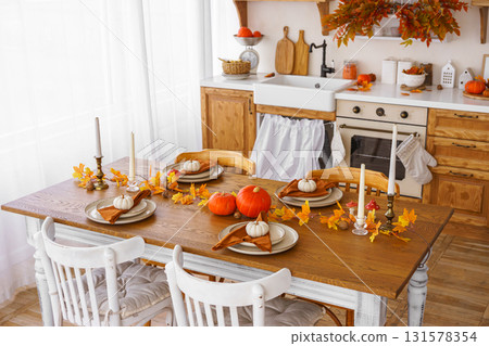 Dining table decorated with pumpkins and fall foliage in a cozy kitchen setting for autumn holiday 131578354