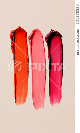 Bright and bold lipstick smears in orange, pink, and magenta are presented side by side on a smooth, neutral surface, highlighting their rich colors 131578529
