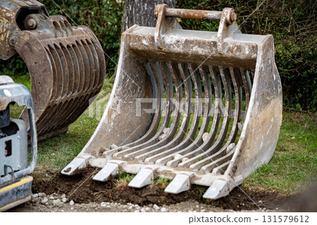 Heavy Excavator Bucket Attached To Yellow Construction Machinery: Dirt Ground And Greenery Background At Worksite 131579612