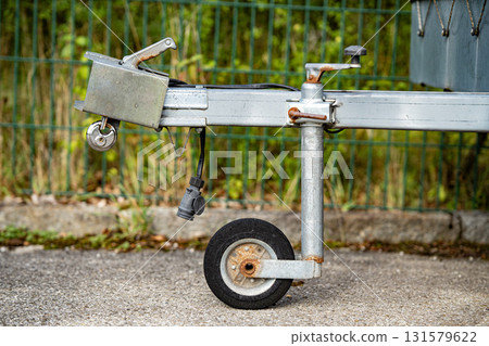 Trailer Hitch Coupling Mechanism On Paved Surface: Close-Up Of Metal Tow Bar With Brake Cable, Rubber Sleeve, And Mounting Hardware For Towing Connection 131579622