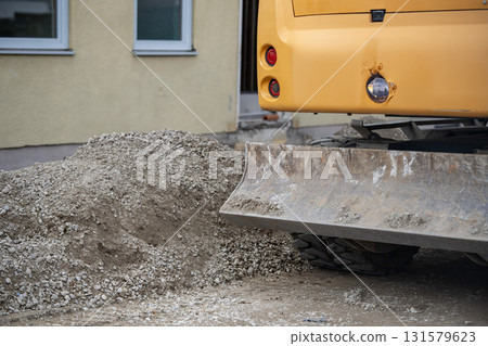 Heavy Excavator Bucket Attached To Yellow Construction Machinery: Dirt Ground And Greenery Background At Worksite Heavy Excavator Bucket Attached To Yellow Construction Machinery: Dirt Ground And Greenery Background At Worksite 131579623