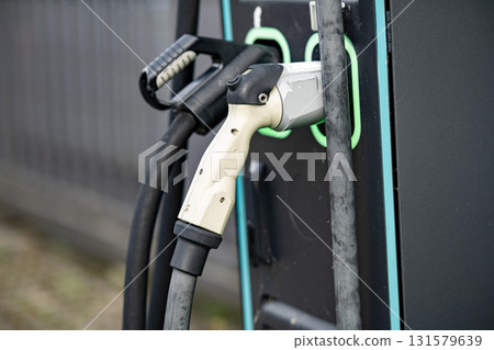 Electric Vehicle Charging Station With Dual Connectors: Close-Up Of Modern EV Power Supply Cables And Sockets With Green LED Outlines On Black Panel In Urban Setting 131579639